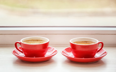 Cups with hot coffee on window sill