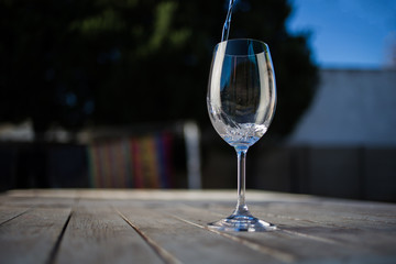 Close up image of wine being poured into a glass on a wooden table outside with natural light