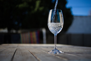 Close up image of wine being poured into a glass on a wooden table outside with natural light