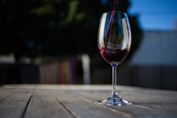 Close up image of wine being poured into a glass on a wooden table outside with natural light