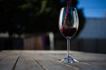 Close up image of wine being poured into a glass on a wooden table outside with natural light