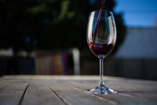 Close up image of wine being poured into a glass on a wooden table outside with natural light