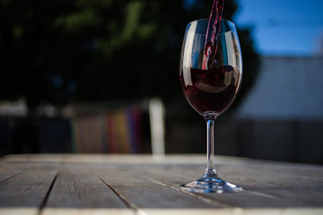 Close up image of wine being poured into a glass on a wooden table outside with natural light