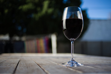 Close up image of wine being poured into a glass on a wooden table outside with natural light