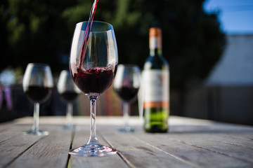 Close up image of wine being poured into a glass on a wooden table outside with natural light