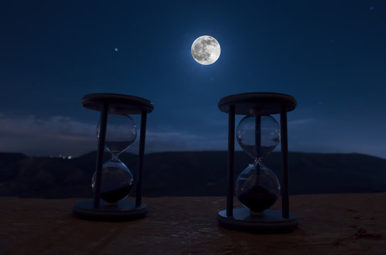 Time concept with a hourglass at night with moon or Sand passing through the glass bulbs of an hourglass measuring the passing time as it counts down to a deadline or closure