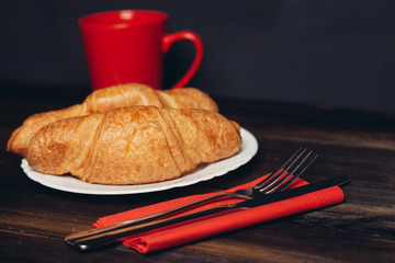 croissants and a red cup, fork and knife on a napkin