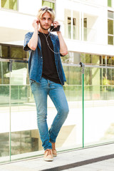 Hipster man standing on city street listening music