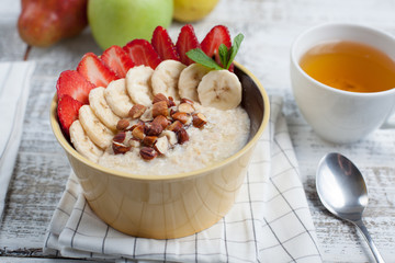 Bowl of oatmeal with a banana, strawberries, almonds, hazelnuts and butter on a rustic table. Hot and a healthy dish for Breakfast, top view