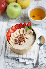Bowl of oatmeal with a banana, strawberries, almonds, hazelnuts and butter on a rustic table. Hot and a healthy dish for Breakfast, top view