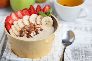 Bowl of oatmeal with a banana, strawberries, almonds, hazelnuts and butter on a rustic table. Hot and a healthy dish for Breakfast, top view