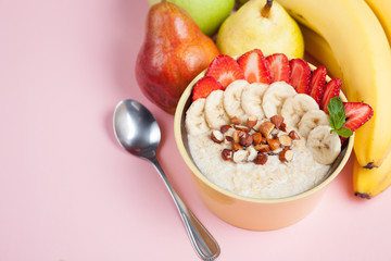 Bowl of oatmeal with a banana, strawberries, almonds, hazelnuts and butter on a pink background. Hot and a healthy dish for Breakfast, top view