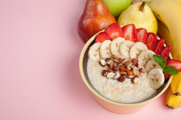 Bowl of oatmeal with a banana, strawberries, almonds, hazelnuts and butter on a pink background. Hot and a healthy dish for Breakfast, top view