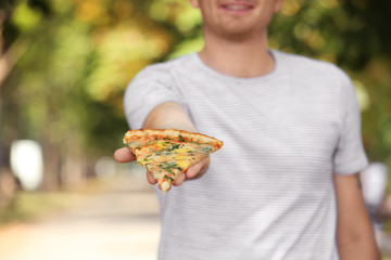 Young handsome man with slice of pizza on blurred natural background