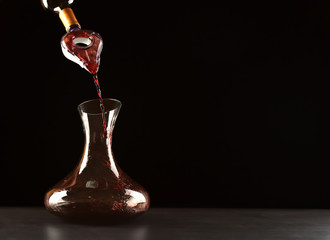 Pouring red wine into decanter on dark background