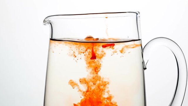 Drops of red liquid dripping into a carafe of water