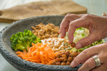 Nice image of a woman's hands preparing a salad in a buddha bowl.
