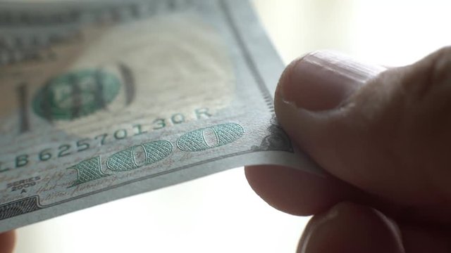 A very close-up of a hundred-dollar bill. Fingers feel the texture of the bill.
