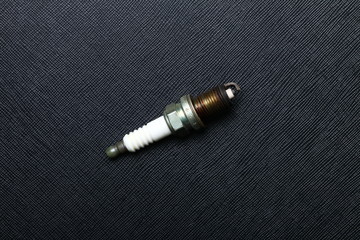 Used and old spark plug after change a new one to engine put on the black color leather surface background  represent the worthless car part condition.