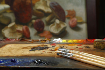 Naklejka premium The workplace of the artist, brushes, paints and canvas. Multicolor oil paints on a palette close up.