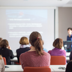 Female speaker giving presentation in lecture hall at university workshop. Rear view of...
