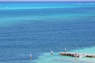 Aerial view on the Caribbean sea shore. One boat is at the docks. Wooden long pier. Turquoise water. Focus point on the pier.