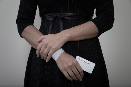 Middle Age Woman In Black Office Dress Showing The Scars Of Self Harm While Holding A Card For Suicide Hotline Number.