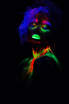 Beautiful extraterrestrial model woman with blue hair and green lips in neon light. It is portrait of beautiful model with fluorescent make-up, Art design of female posing in UV with colorful make up