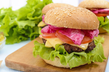 Hamburgers with juicy cutlet, tomatoes, pickled cabbage and cucumbers, cheese, green lettuce leaves and a soft bun with sesame