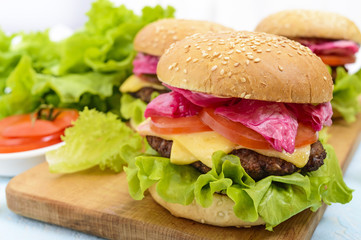Hamburgers with juicy cutlet, tomatoes, pickled cabbage and cucumbers, cheese, green lettuce leaves and a soft bun with sesame