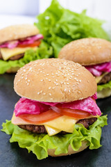 Hamburgers with juicy cutlet, tomatoes, pickled cabbage and cucumbers, cheese, green lettuce leaves and a soft bun with sesame