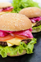 Hamburgers with juicy cutlet, tomatoes, pickled cabbage and cucumbers, cheese, green lettuce leaves and a soft bun with sesame