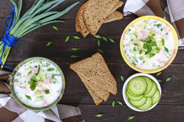 Light diet soup with fresh cucumbers, seasoned with yogurt in ceramic bowls on dark wooden background. Traditional Russian dish - "okroshka". The top view.