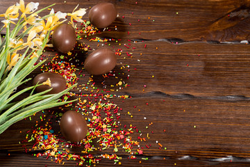 Beautiful Easter composition with chocolate eggs, colored powder for cakes on old brown wooden background