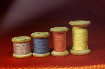 Old wooden coils of thread on an orange red fabric on a black background close up