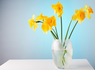 Narcissuses in a glass vase on a white table.