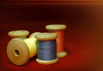 Old wooden coils of thread on an orange red fabric on a black background close up