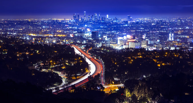 Los Angeles city skyline and highway 101 viewed from West Hollywood hills or heights. Trails of light from cars and traffic.
