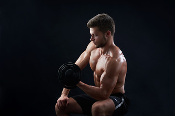 Fototapeta na wymiar Muscular young shirtless man with toned and ripped body working out with dumbbells lifting weights on black background copyspace gym athlete sportsman sport effort determination health strength.