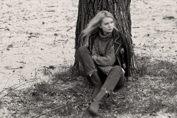 

Young sexy stylish blonde girl in nature near a river and trees in American country style in a leather jacket, sweater blue jeans and brown boots with a beautiful face and pretty eyes
