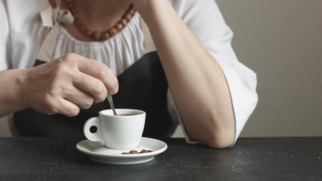 Front view of woman in the apron stir the sugar in small cup of hot coffee at home.