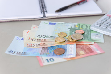 Euro money banknotes and coins counting with calculator, note book and pen on desk