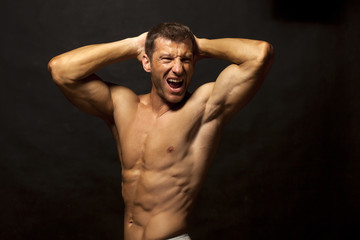 Fototapeta premium half-naked handsome and muscular young man posing on a dark background