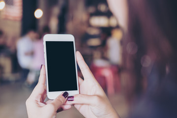 Mockup image of a woman holding white mobile phone with blank white screen in modern loft cafe