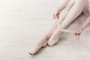 Ballerina puts on pointe ballet shoes, graceful legs - obrazy, fototapety, plakaty