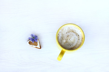 Favorite warming fragrant breakfast/ Foamy cappuccino in a yellow mug, with a gingerbread and spring flower top view