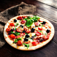 Hot pizza with meat, basil and mozarella cheese on a dark background, top view. Pizza on the rustic wooden  table with copy space.