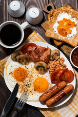 Fried eggs with bacon, sausages and vegetables for breakfast, vertical top view