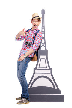 Travel concept. Full length studio portrait of happy handsome young man standing near Eiffel tower. Isolated on white.