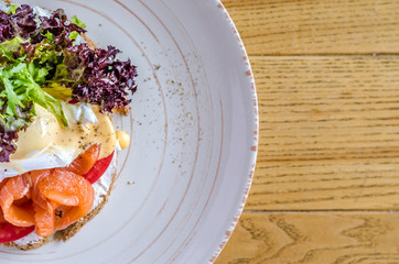 Sandwich with red fish cheese and herbs on a plate, on a wooden table, view from above